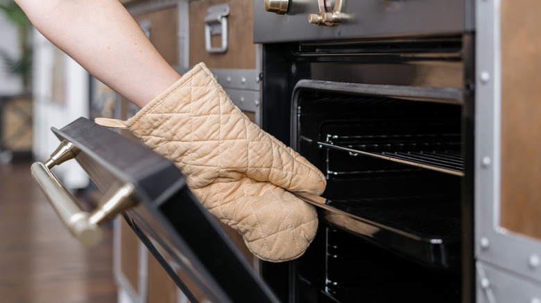 Person wearing a tan oven mitt reaching into an open oven.
