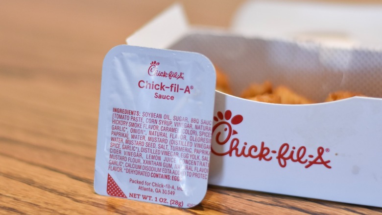 A container of Chick-fil-A sauce in front of a box of nuggets on a wooden table