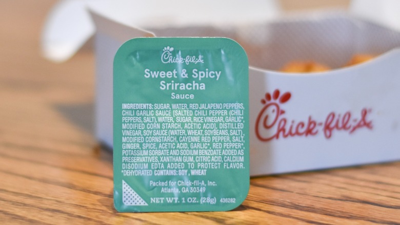 A container of sweet and spicy sriracha sauce in front of a box of nuggets on wooden table