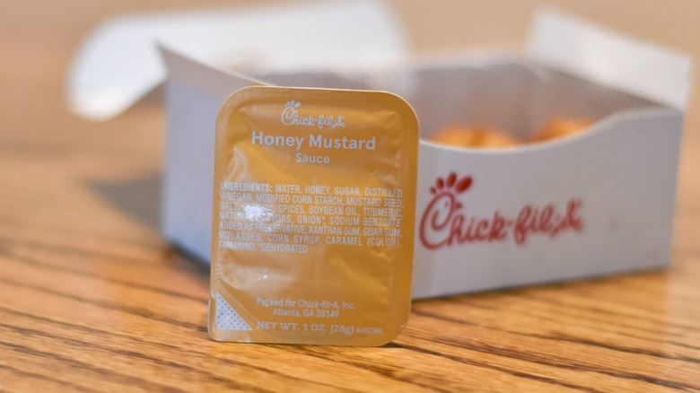 A container of honey mustard in front of a box of nuggets on a wooden table