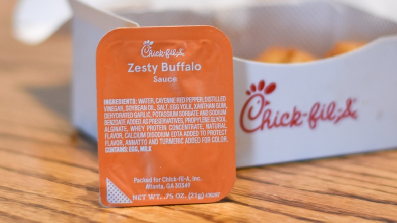 A container of zesty buffalo sauce in front of a box of nuggets on a wooden table