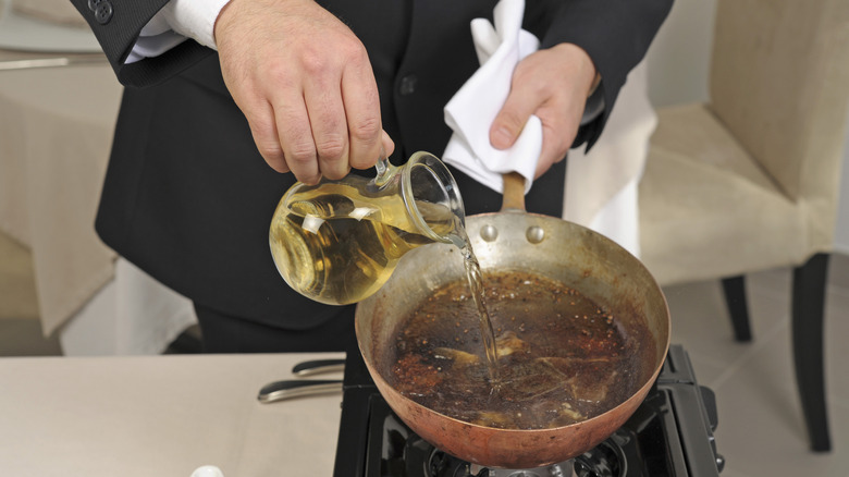 Person deglazing a pan with white wine vinegar