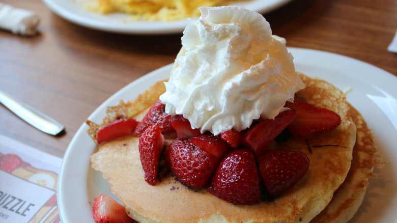 Stack of pancakes with whipped cream and strawberries