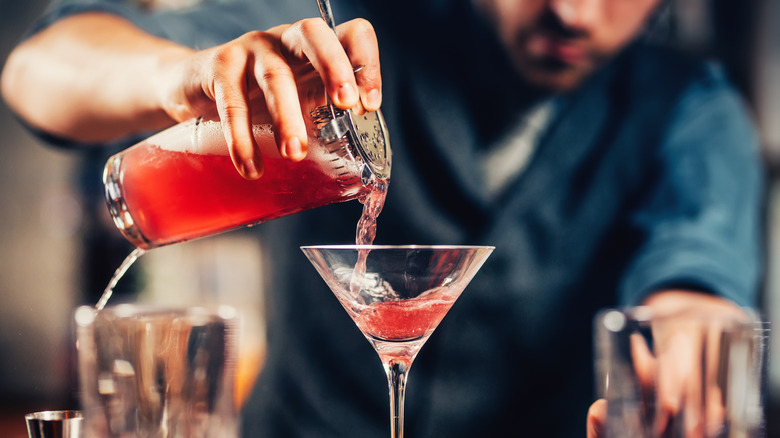 Bartender pouring red cocktail into martini glass