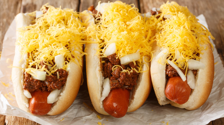 Three Cincinnati style hot dogs are piled high with cheese.