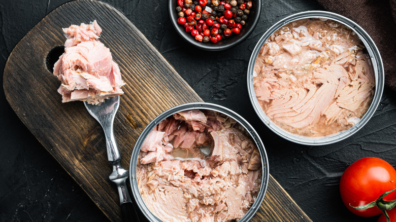 Open cans of chunk tuna and tuna on a fork