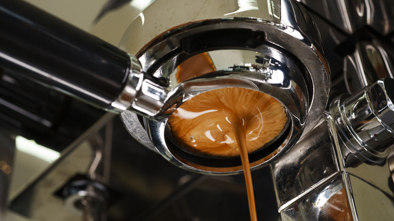 the underside of an espresso machine with a shot of caramel colored espresso being pulled