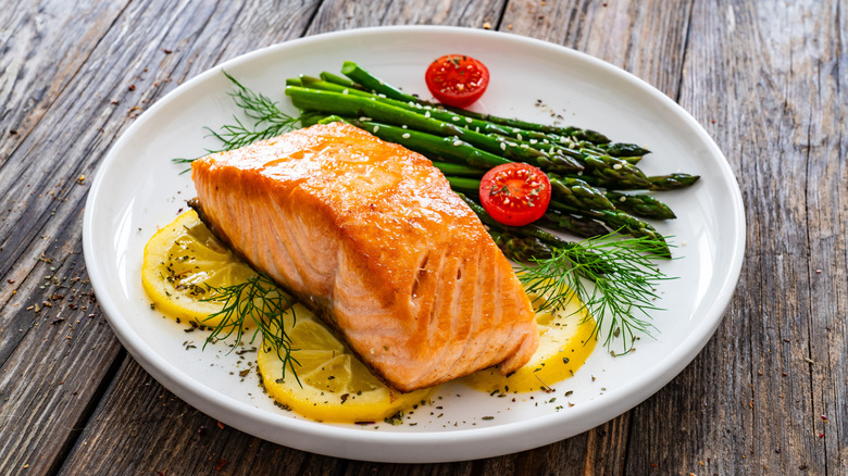 A plate of baked salmon, roasted asparagus, Cherry tomatoes, lemons, and herbs.