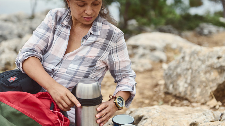 Sitting person handling a thermos in the outdoors