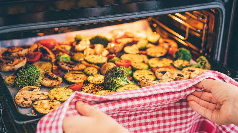 Woman putting tray of vegetables in oven