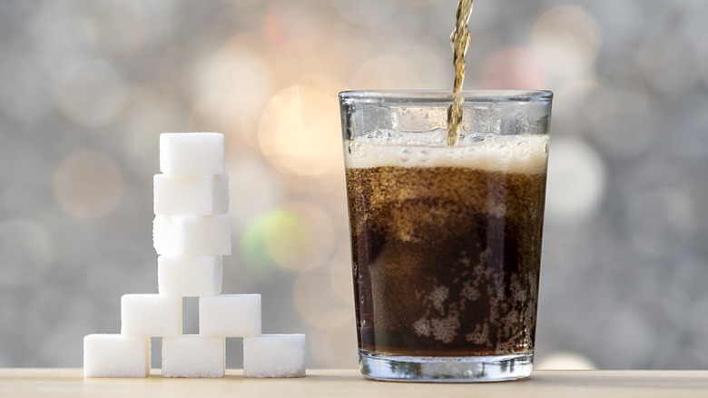 a glass of soda next to a stack of sugar cubes