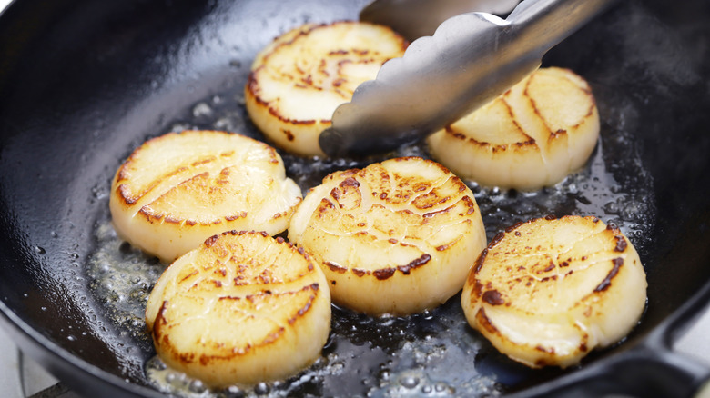 Tongs turning scallops in pan