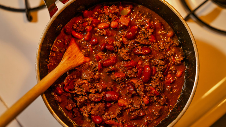 Pot of chili sitting on a stove top with a wooden spoon.