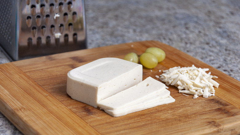 Grapes and vegan mozzarella on a wooden cutting board next to grater