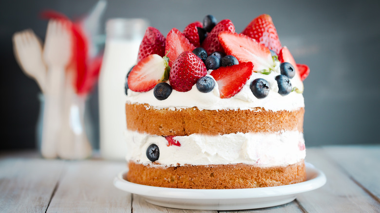 A layer cake has thick clouds of whipped cream and topped with berries.