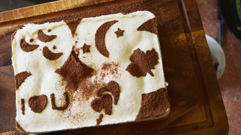 A tiramisu with stenciled images sits on a wood board.