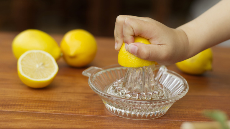A hand squeezing a lemon on a glass lemon juicer