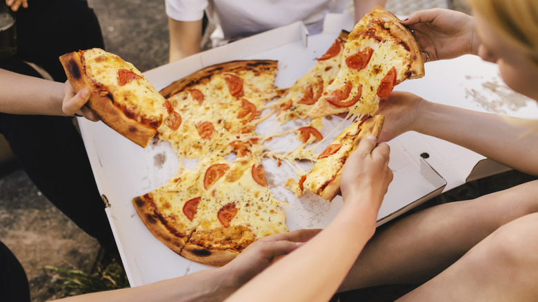 people pulling out slices of takeout pizza from a box