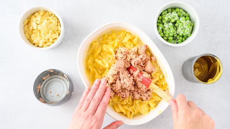 Person mixing tuna casserole ingredients in dish