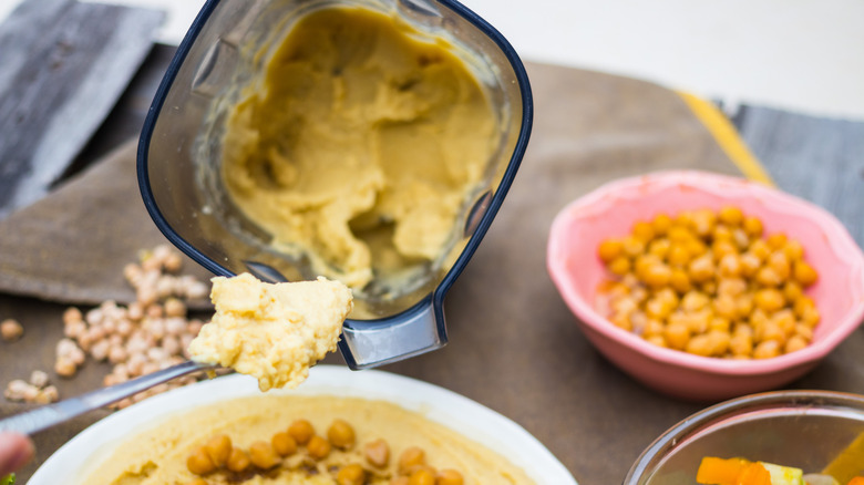 A spoon holding hummus from a blender