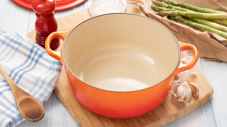 An orange enameled cast iron pot on a cutting board