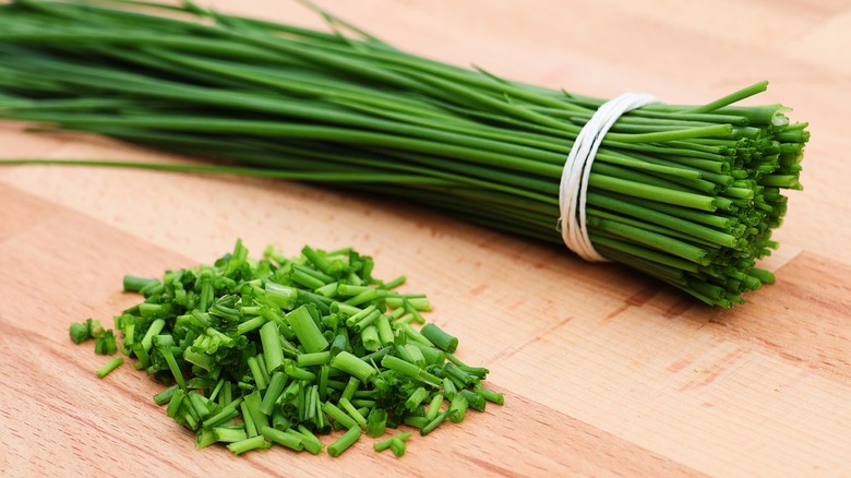 Fresh bunched and sliced chives on wooden cutting board