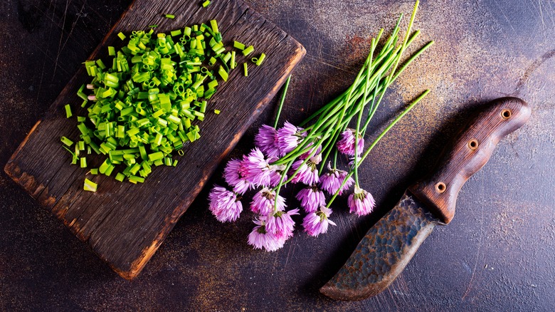 Chopped chives and chive flowers with a rustic knife