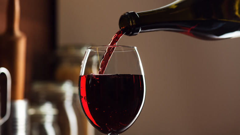 Red wine being poured from a bottle into a stemmed wine glass.