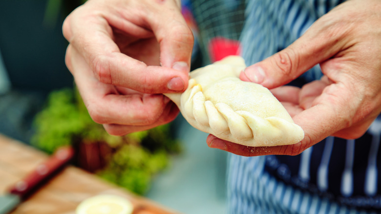 Hands demonstrating empanada crimping technique