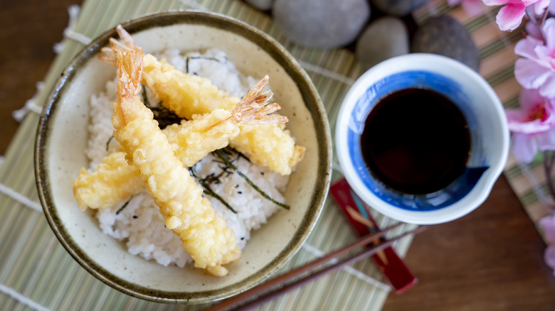 Tempura shrimp with dipping sauce is displayed with chopsticks.