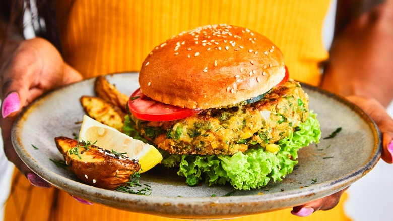 A woman holds a veggie burger on a plate