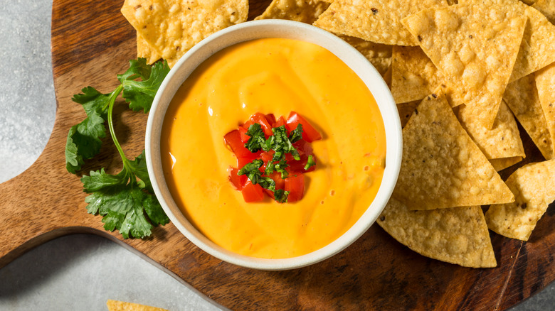 Nacho cheese with tortilla chips on cutting board