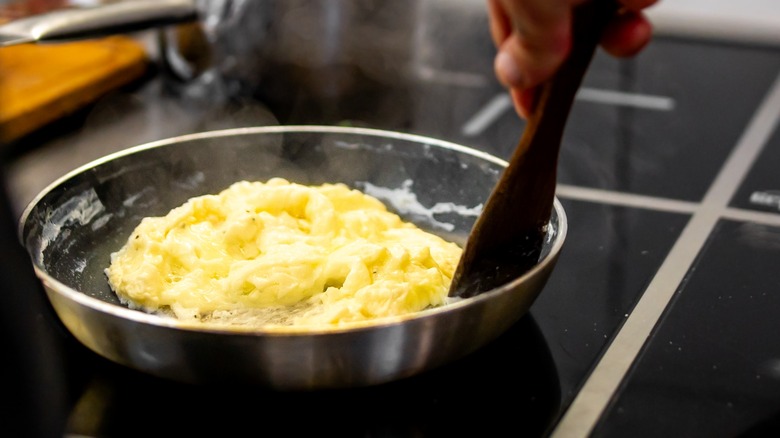 Person scrambling eggs in a pan on a stovetop