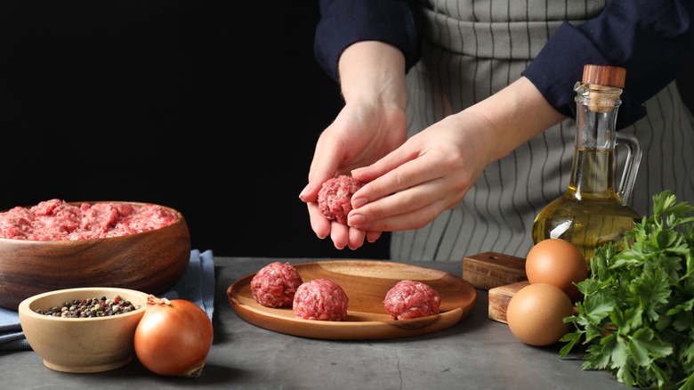 woman shaping ground meat into meatballs with other ingredients on table