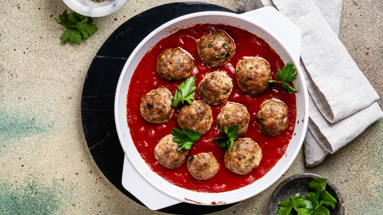 meatballs in a white pot with red sauce and herbs
