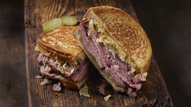 a grilled pastrami sandwich with pickles on the side