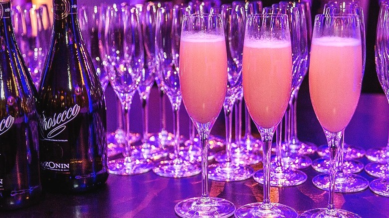 Bellini cocktails are lined up next to bottles of prosecco.