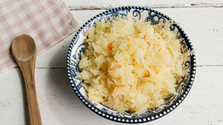 A bowl of sauerkraut next to a wooden spoon