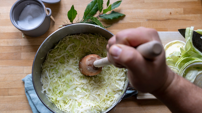 Closeup of a hand mixing salt into a bowl of shredded cabbage to make sauerkraut