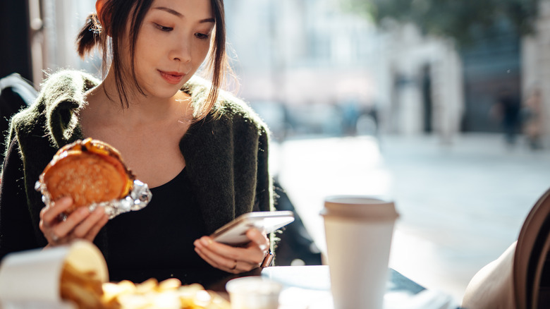 Woman eating fast food breakfast while checking her phone