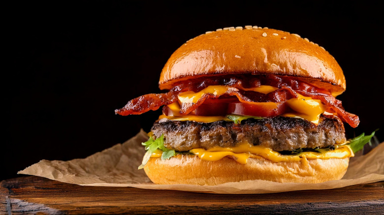 A cheeseburger with bacon is in front of a black background.