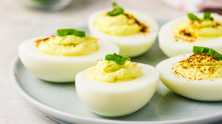 deviled eggs garnished with chives and paprika sit on a gray plate