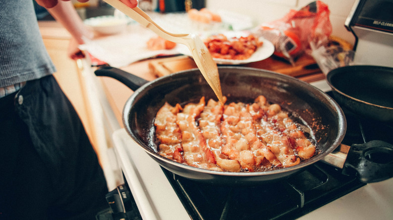 Person frying bacon on the stove