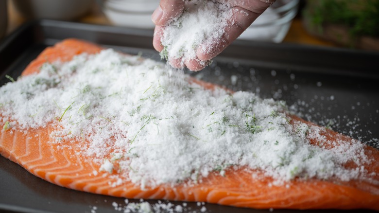 A hand applying a salt and sugar cure to salmon