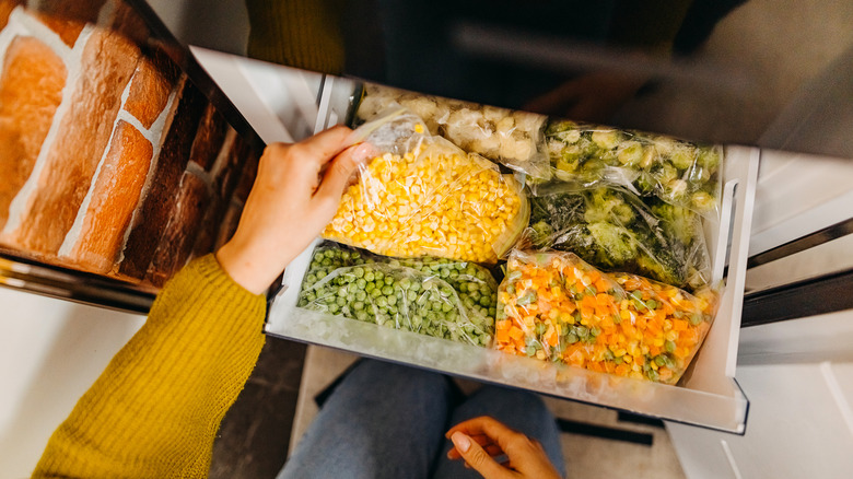 Hand holding bags of frozen vegetables in a freezer drawer