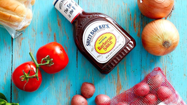 Bottle of Sweet Baby Ray's Barbecue sauce surrounded by whole vegetables on a worn blue wooden table