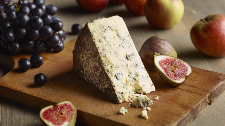 A wedge of blue cheese on a wooden board with fresh fruit