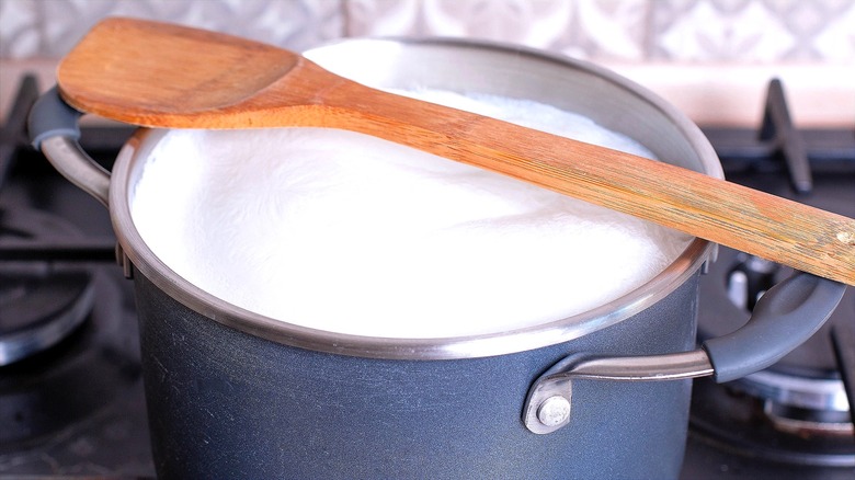 Pot of milk heating over the stove with a wooden spoon across the top