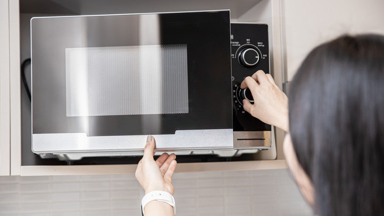 A person is seen from behind operating a microwave.