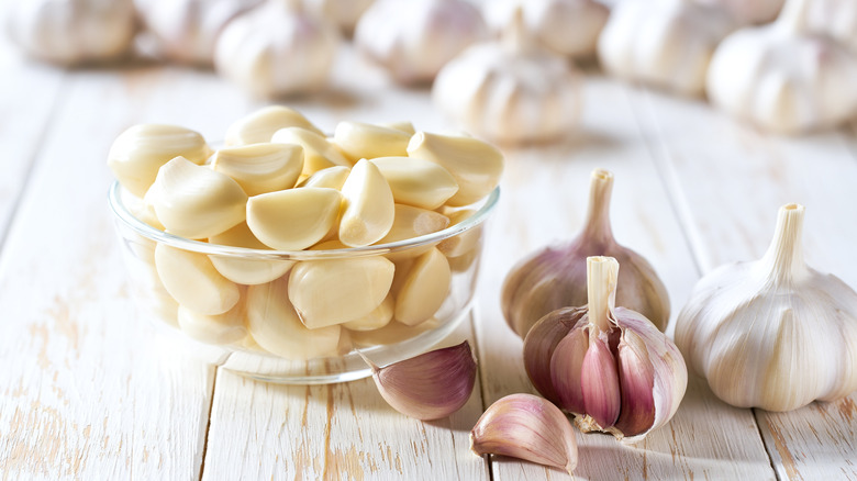 Peeled garlic in a glass bowl with garlic bulbs around it